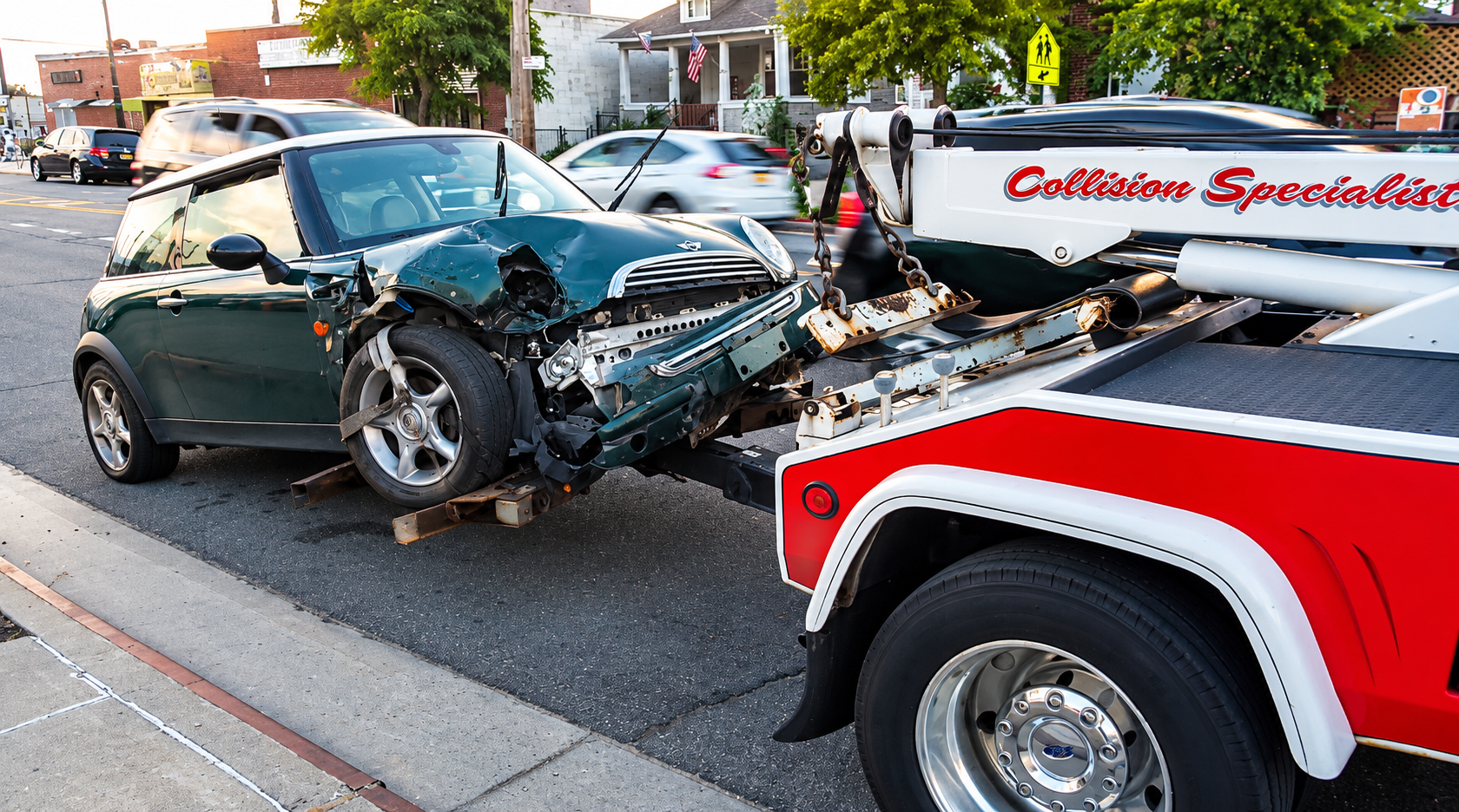 Severely damaged green car after a collision with a red tow truck on a street.