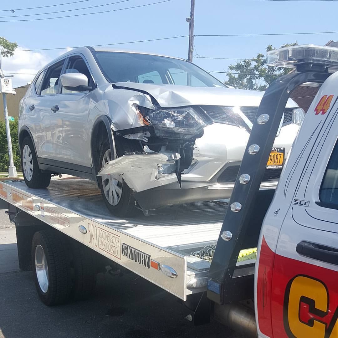 Damaged silver SUV on a tow truck after a front-end collision, with a white service vehicle beside it.