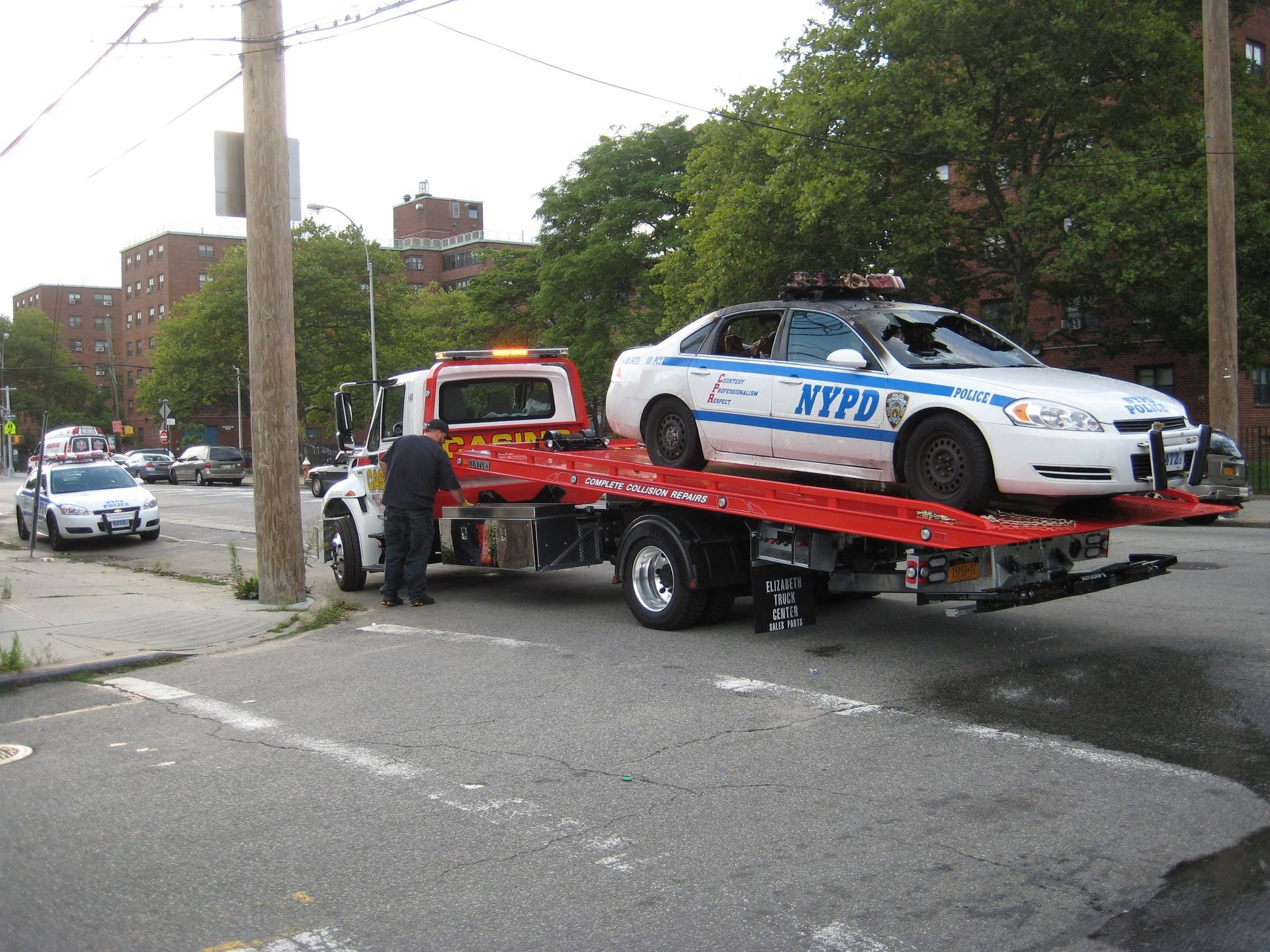 Tow truck hauling an NYPD police car on a city street after an apparent accident