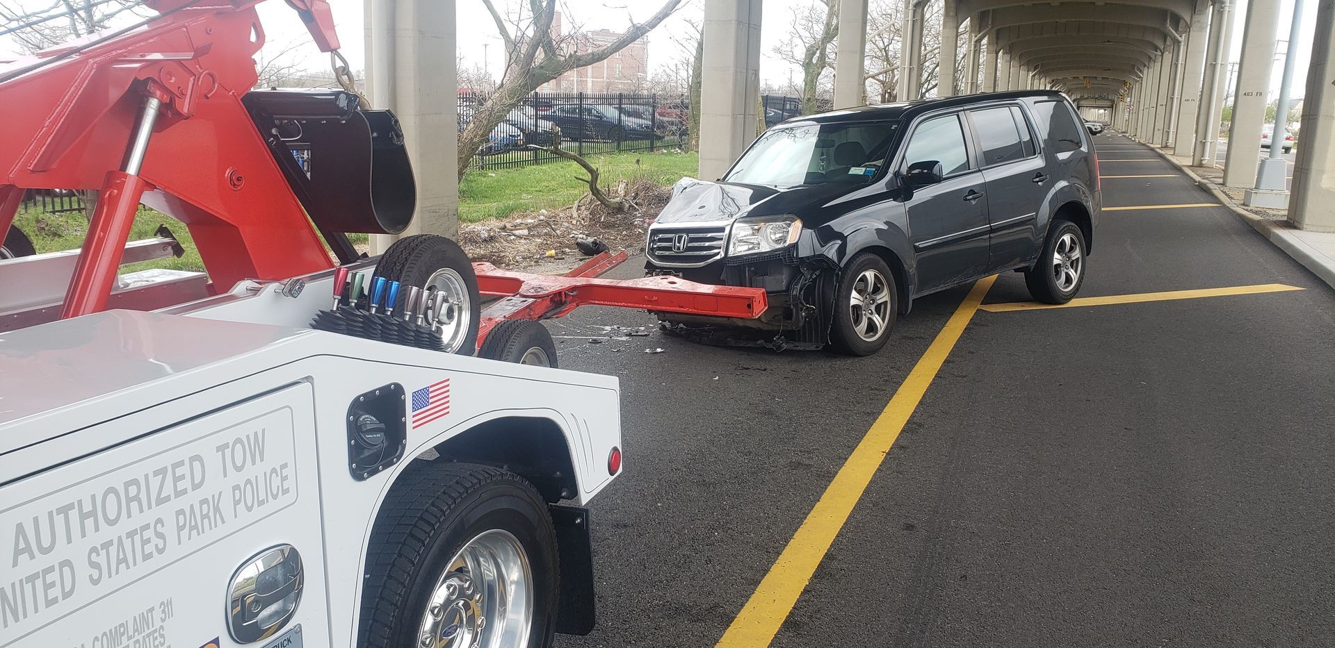 Tow truck loading a damaged gray SUV on a road under an overpass