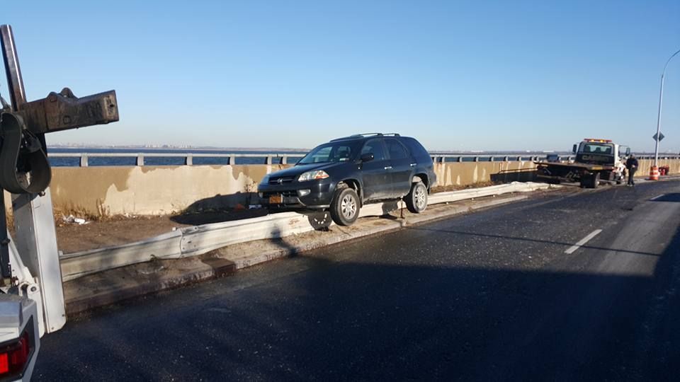 SUV stopped on a bridge shoulder beside a concrete barrier, with another vehicle in the distance.
