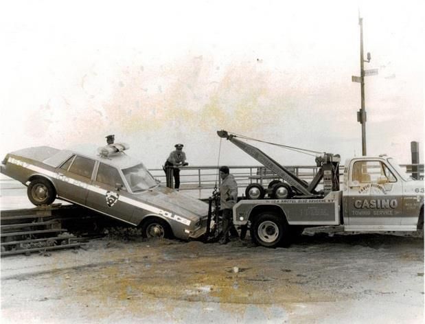 Tow truck lifting a silver car from a wet road beside a casino in a snowy scene