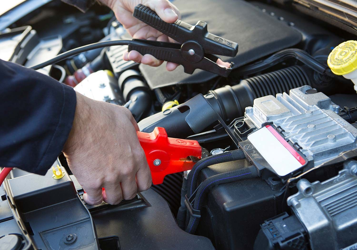 Hands using jumper cables to connect a car battery in an engine bay