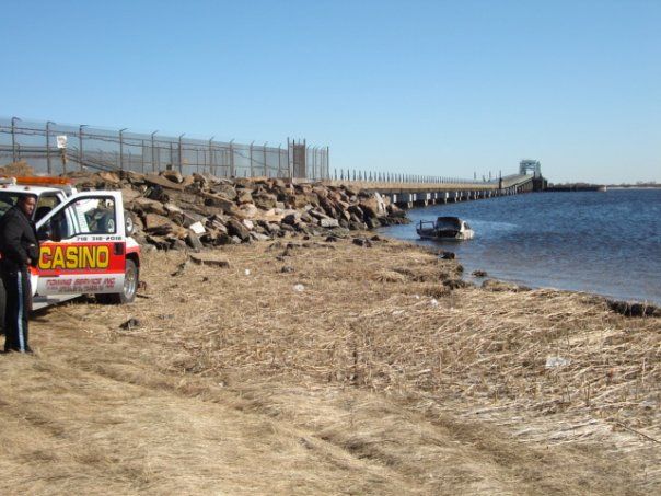 Rocky shoreline with a red construction vehicle and seawall beside calm water under a clear sky