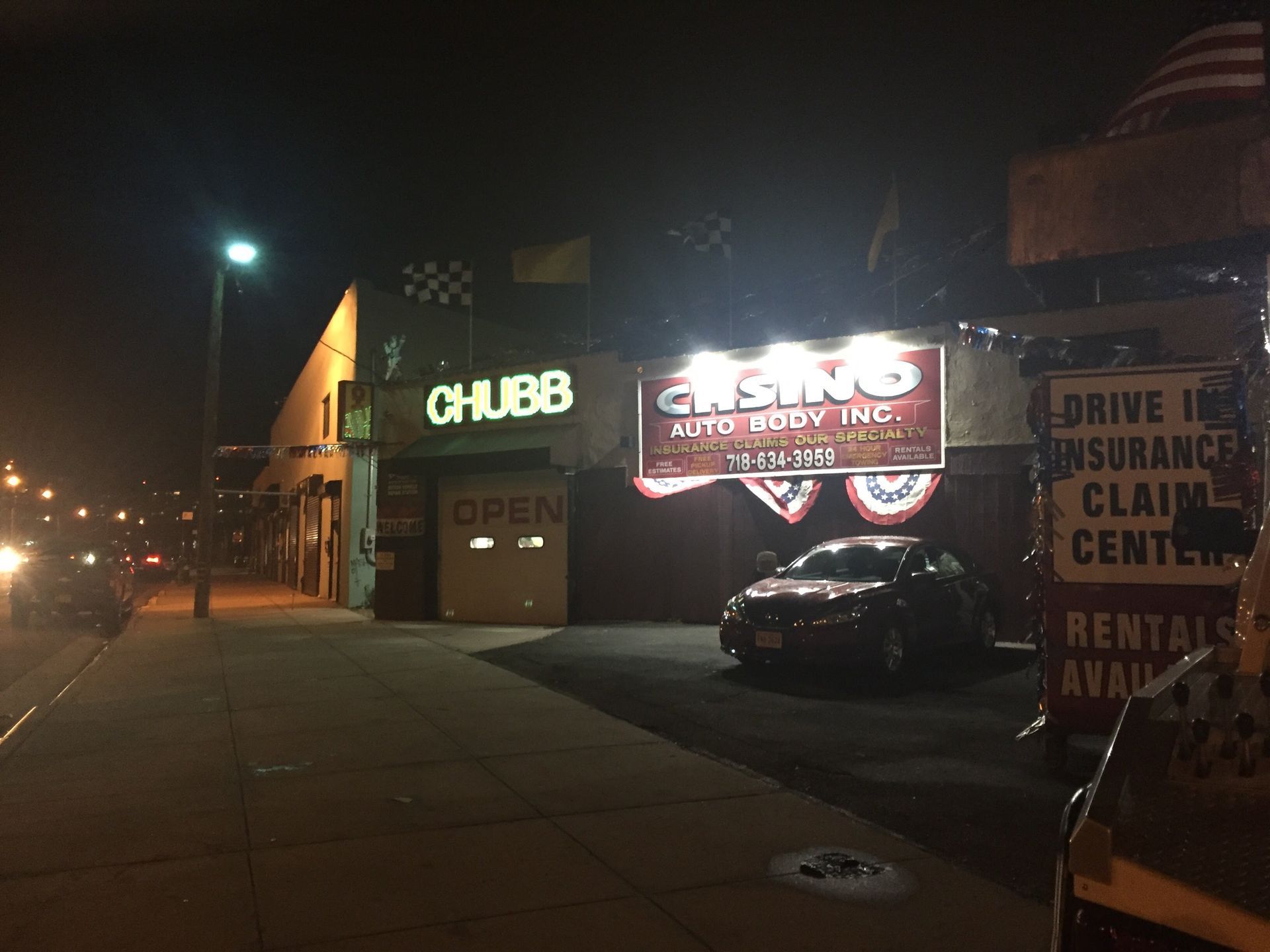 Nighttime storefronts with bright signs, a parked car, and a sidewalk on a city street.
