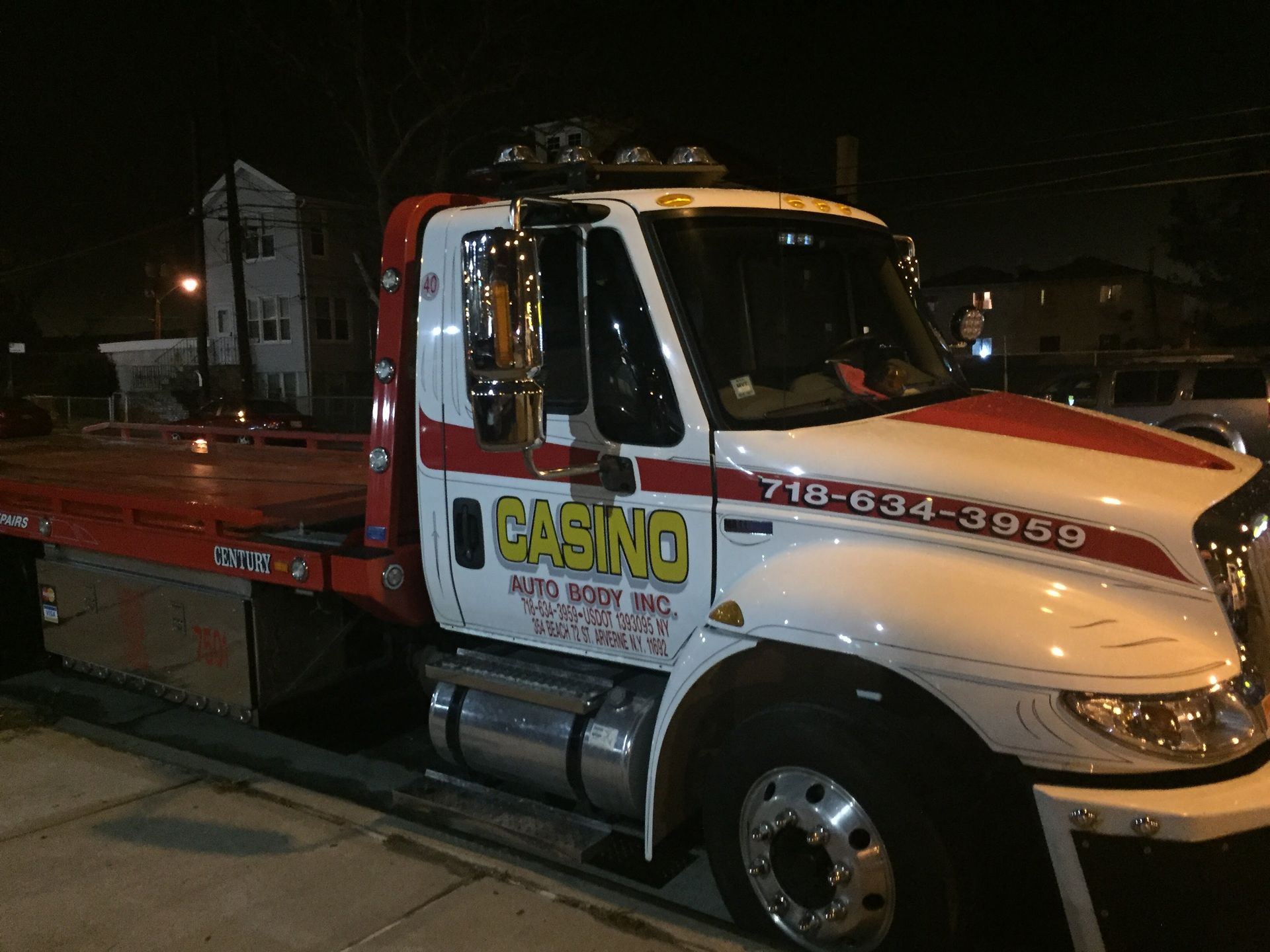 Tow truck parked at night with red flatbed and white cab, roadside scene with company logo on door