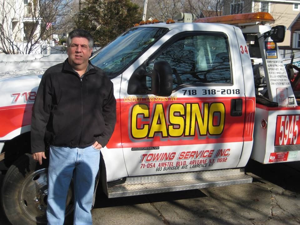 Tow truck with “CASINO TOWING SERVICE” lettering parked beside a man in black jacket and jeans