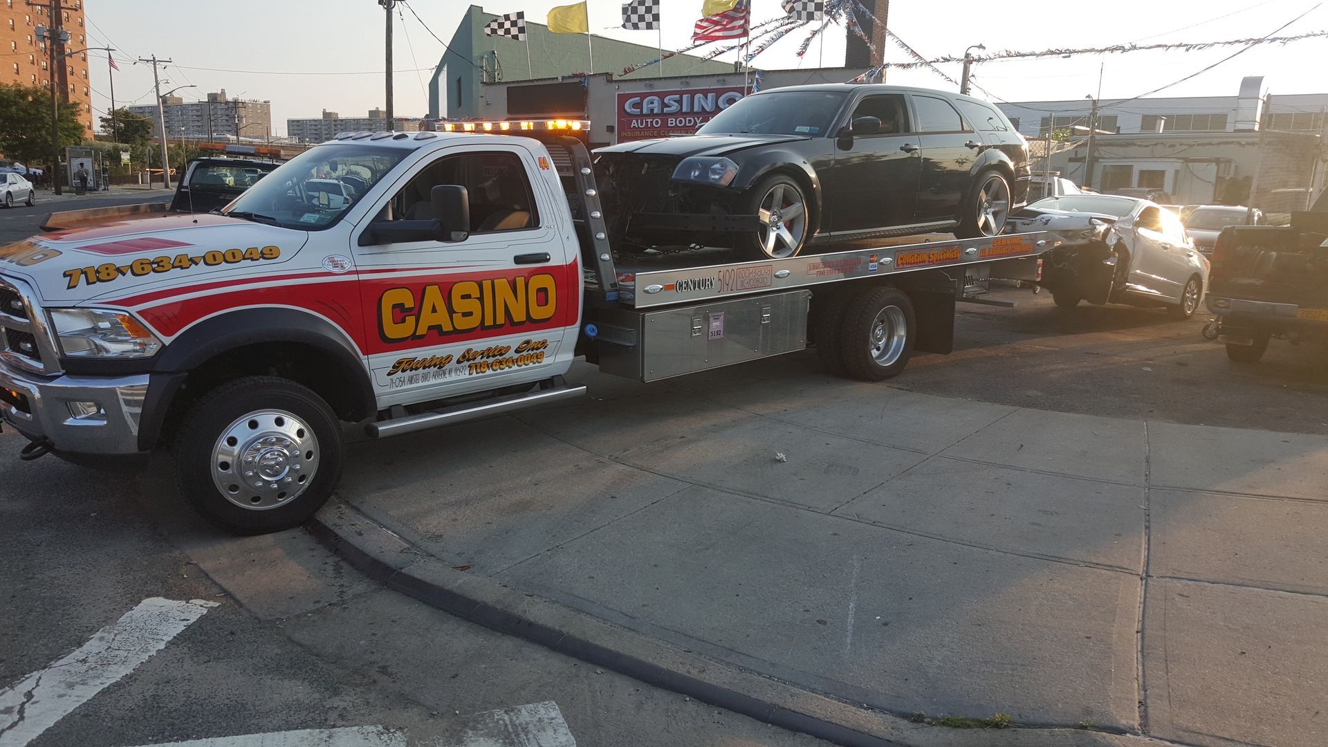 Tow truck hauling a black car on a flatbed at sunset outside a casino lot