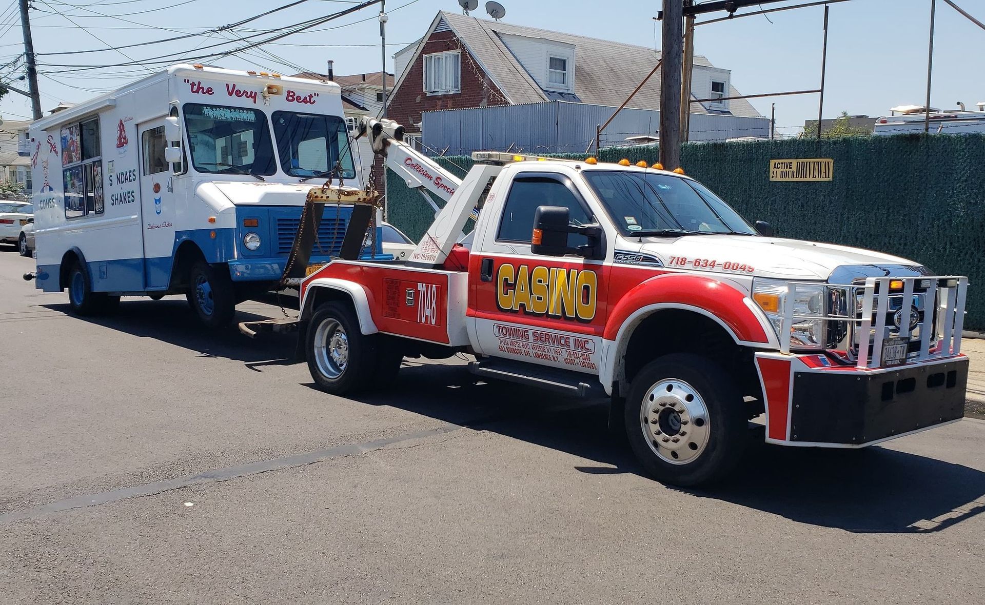 Red tow truck towing a white-and-blue truck on a street near houses