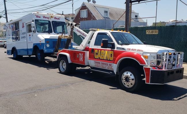 Red tow truck towing a white-and-blue truck on a street near houses