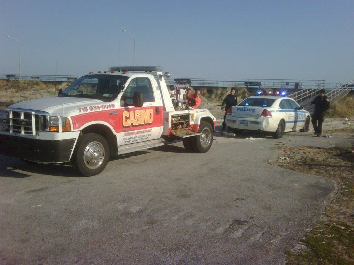 Tow truck towing a police car on a roadside, with officers nearby.