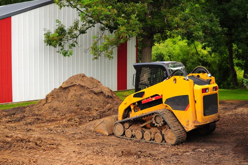 A small excavator bucket scoops up dirt in an outdoor setting.