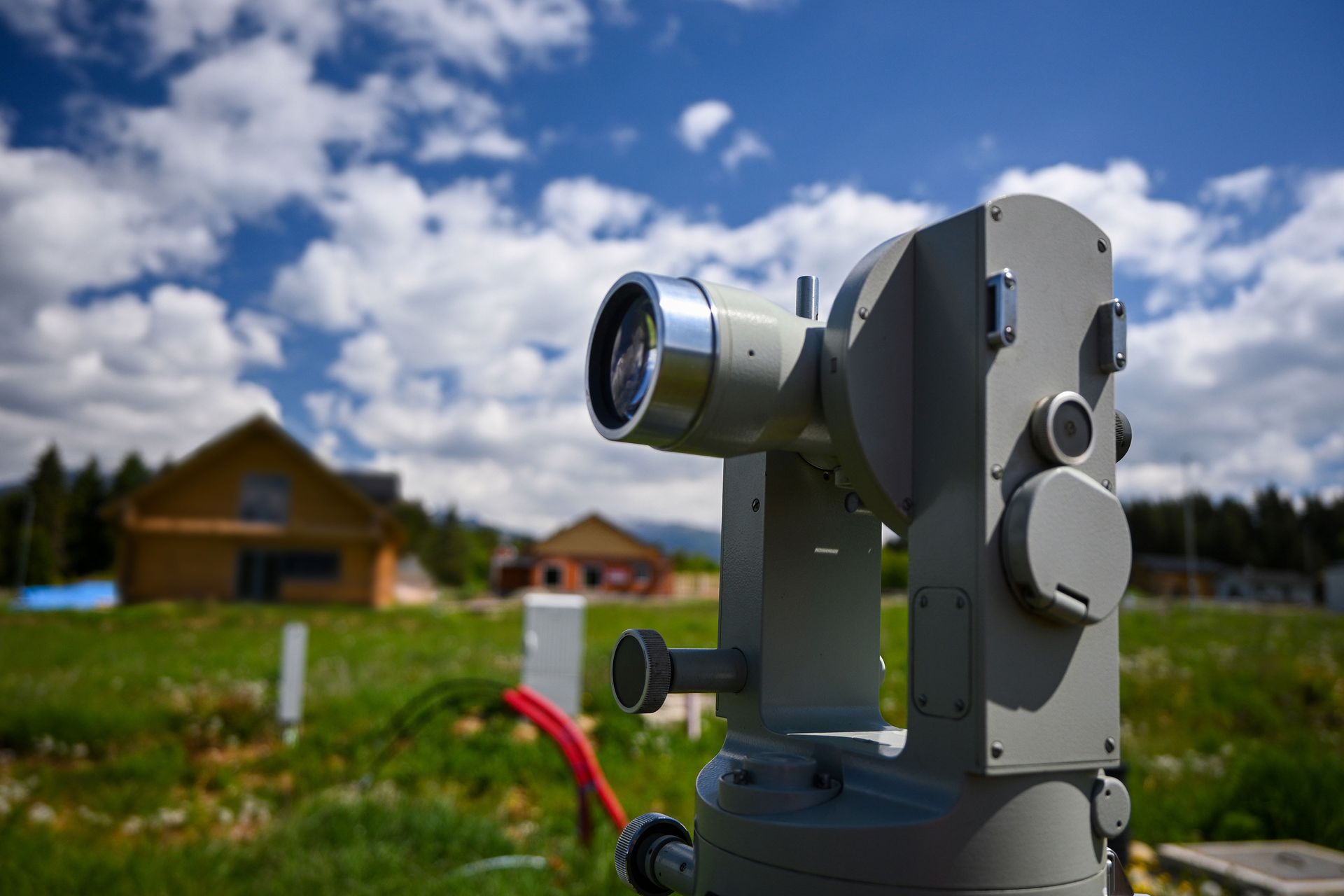 Silver survey instrument on a tripod in a grassy field with houses in the background Silver survey instrument on a tripod in a grassy field with houses in the background
