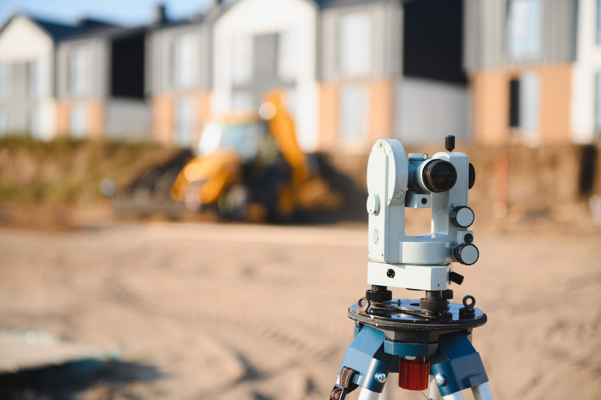 Surveying instrument on tripod at a construction site with houses in the background Surveying instrument on tripod at a construction site with houses in the background