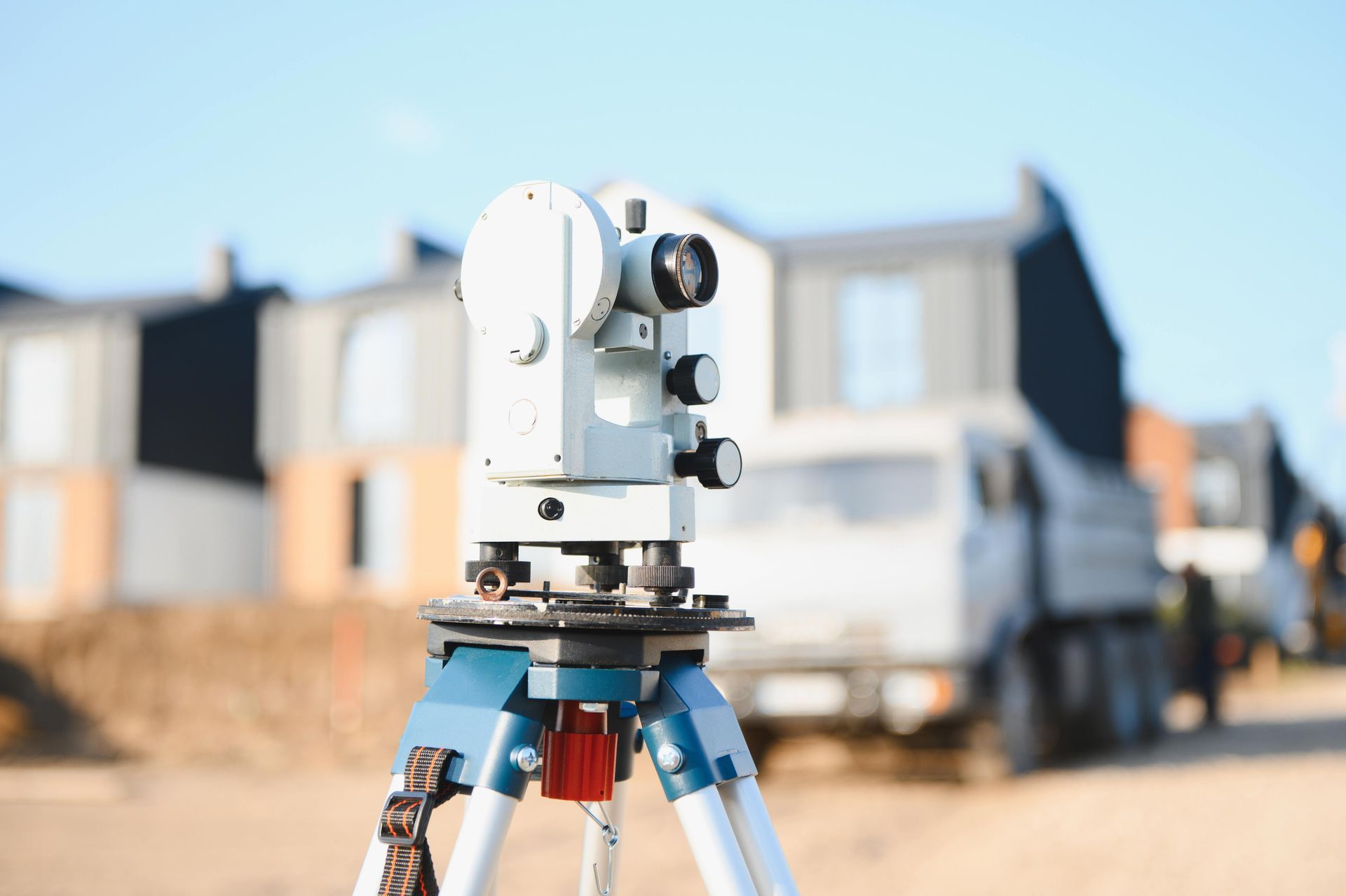 Surveying instrument on a tripod in front of a construction site and truck Surveying instrument on a tripod in front of a construction site and truck