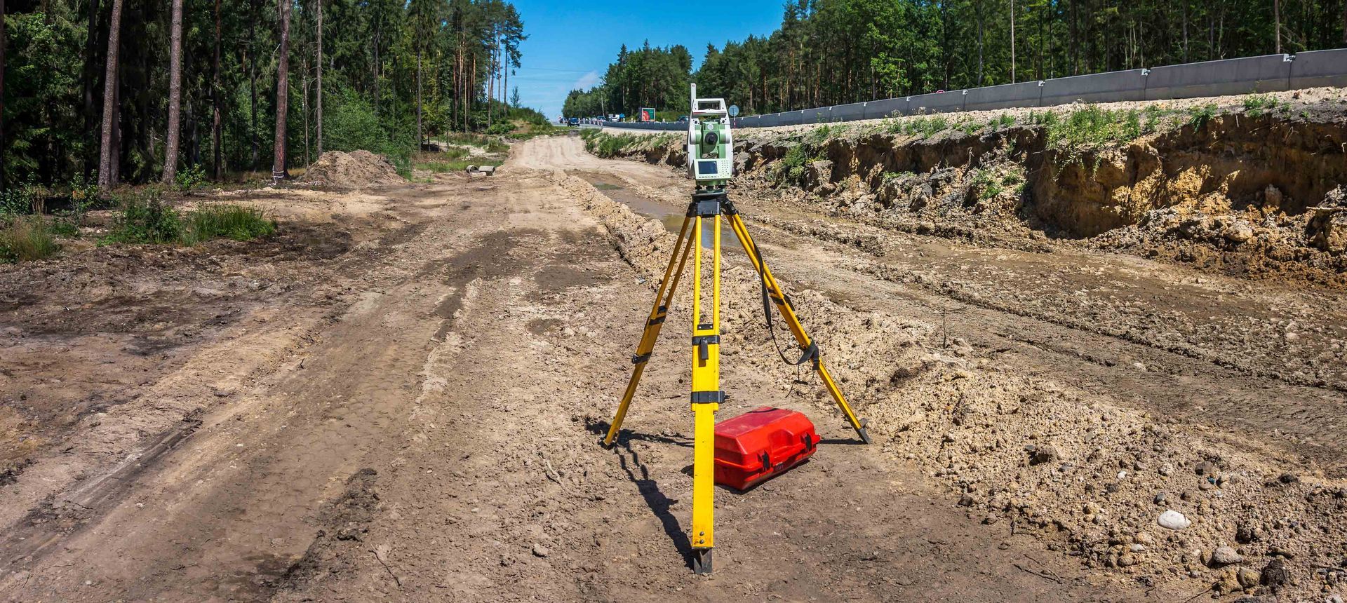 Survey tripod with yellow legs on a dirt road in a forest clearing, marking a construction site. Survey tripod with yellow legs on a dirt road in a forest clearing, marking a construction site.