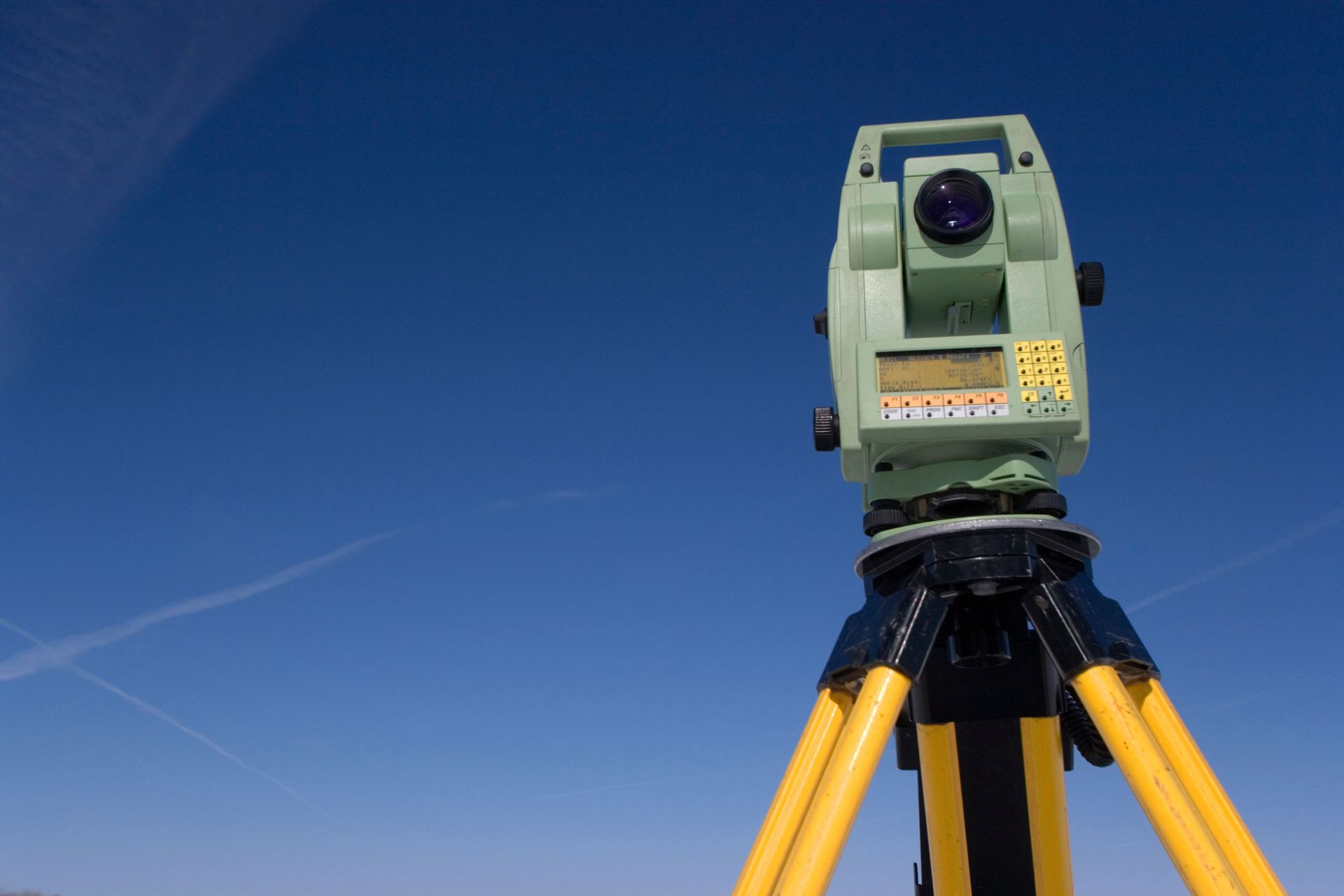 Surveying instrument on a yellow tripod against a clear blue sky.