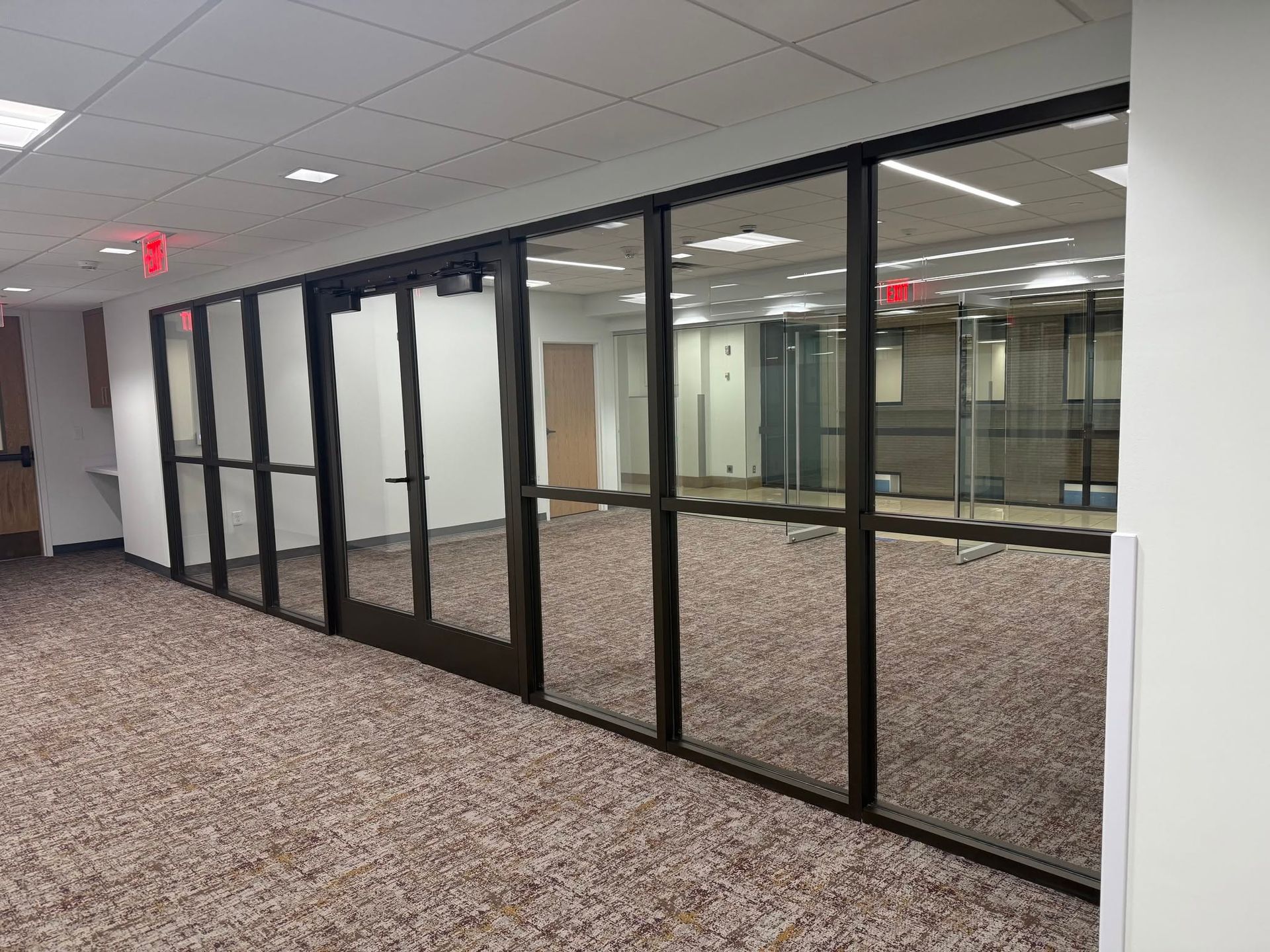Empty office hallway with black-framed glass walls and carpeted floor.