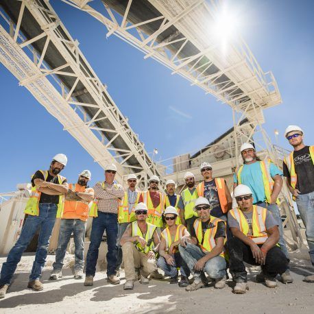 Construction crew in hard hats and safety vests posing beneath a steel framework at a worksite