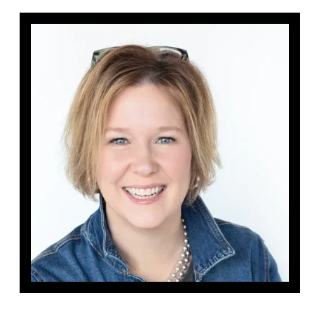 A woman wearing a denim jacket and a pearl necklace is smiling.