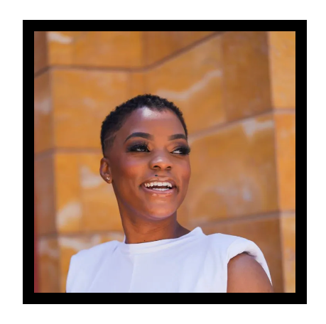 A woman in a white top is smiling in front of a yellow wall.