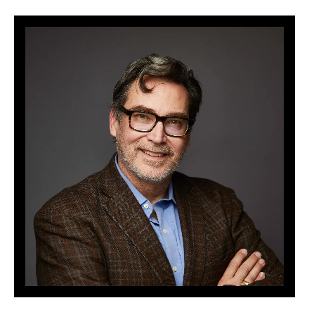 A man with a beard is wearing a suit and a blue shirt.