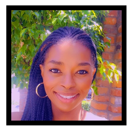 A woman with braids and hoop earrings is smiling in front of a brick wall.
