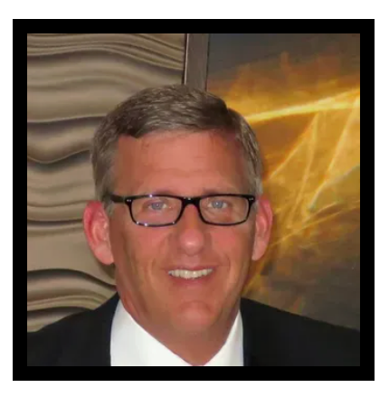 A man wearing glasses and a suit and tie is smiling.