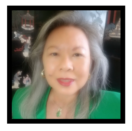 A woman with gray hair is wearing a green jacket and a green necklace.
