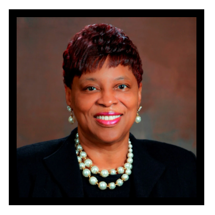 A woman wearing a pearl necklace and earrings is smiling for the camera.
