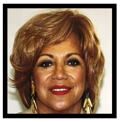 A woman wearing a tan jacket and gold earrings smiles for the camera