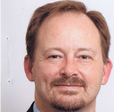 A man with a beard is wearing a suit and a blue shirt.