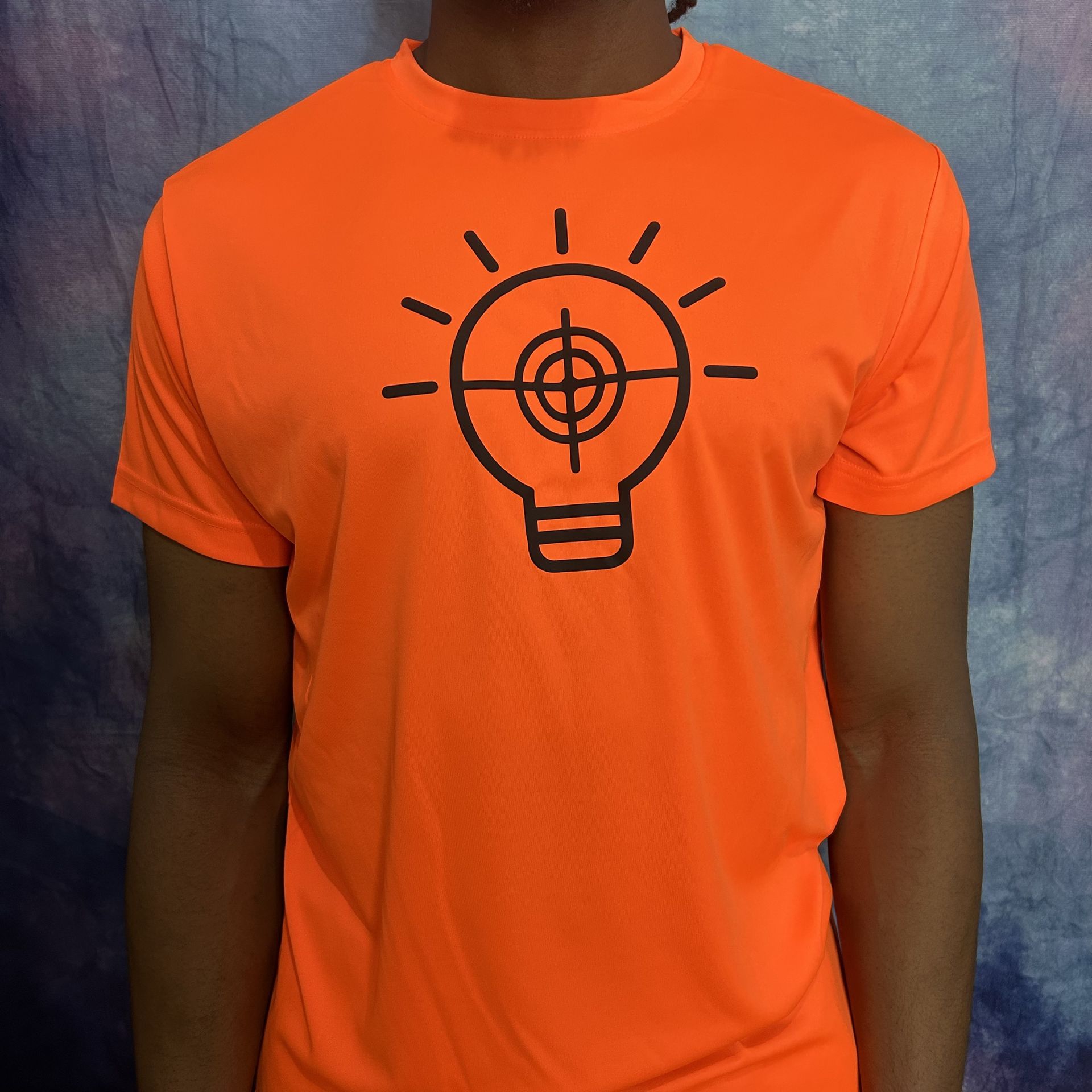 Orange t-shirt with a black graphic of a lightbulb with a target in the center.