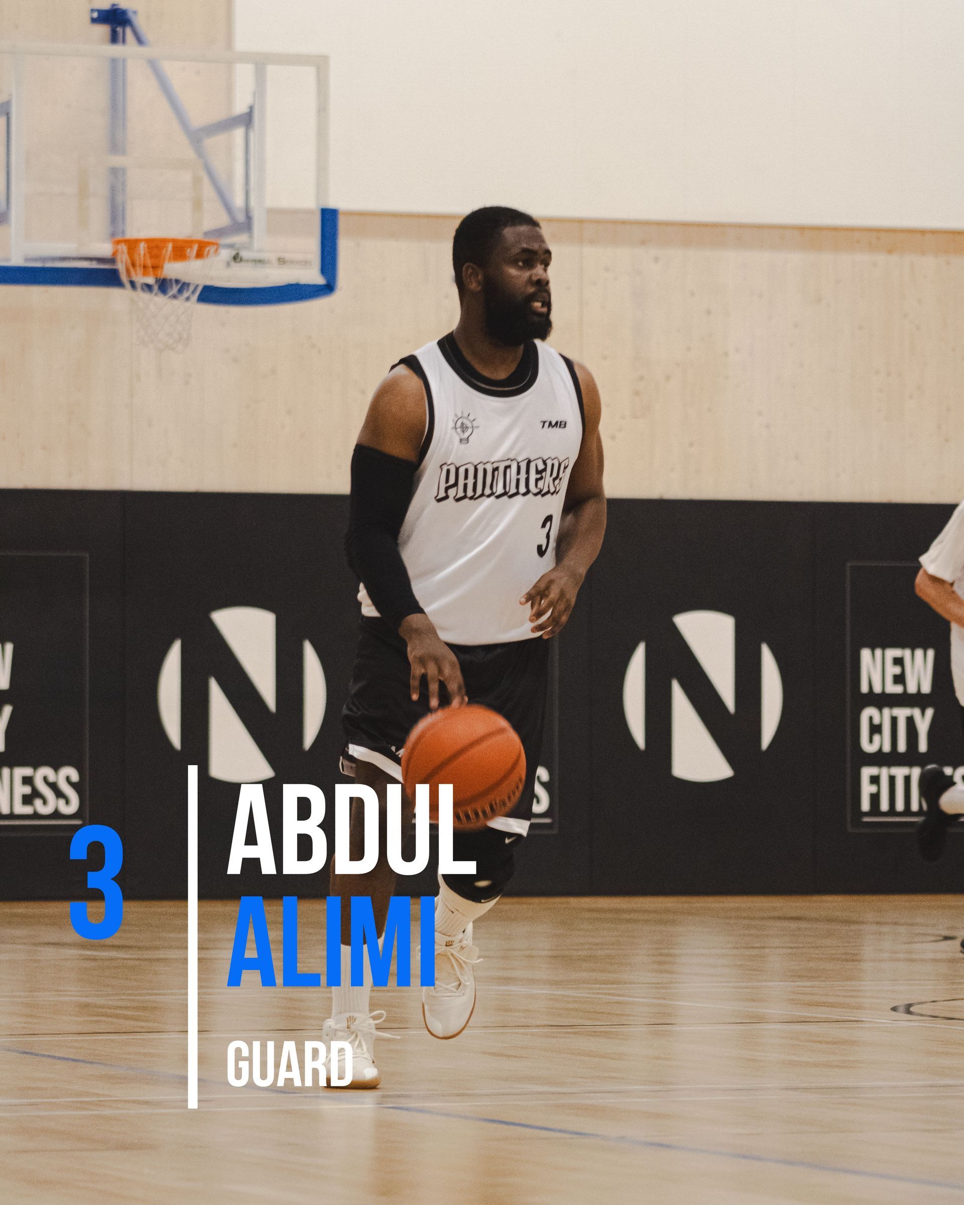 Basketball player Abdul Alimi dribbling the ball on a court. He wears a jersey and is looking to the side.