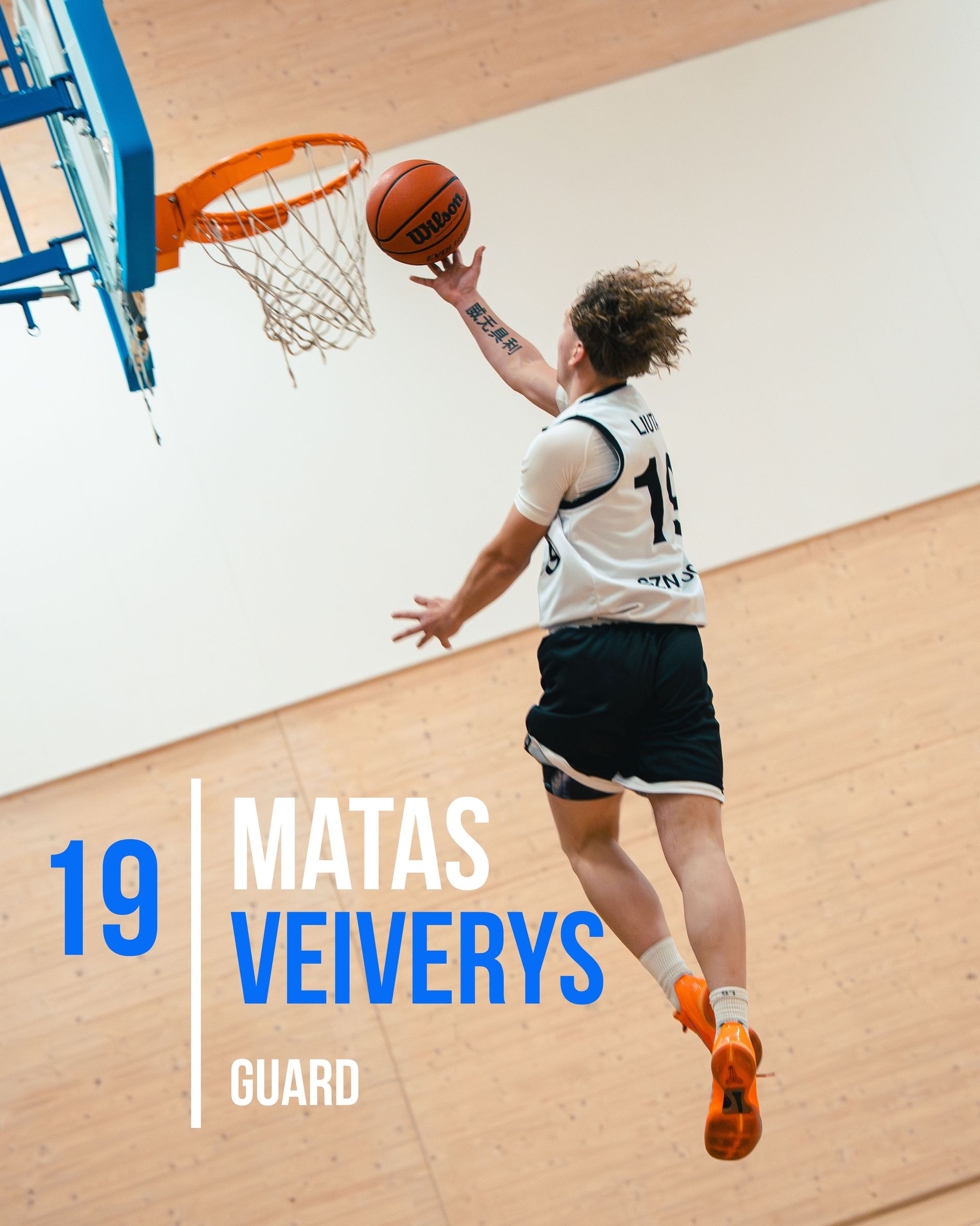 Basketball player Matas Veivery, number 19, shoots a layup. Orange ball, blue rim, and white wall.