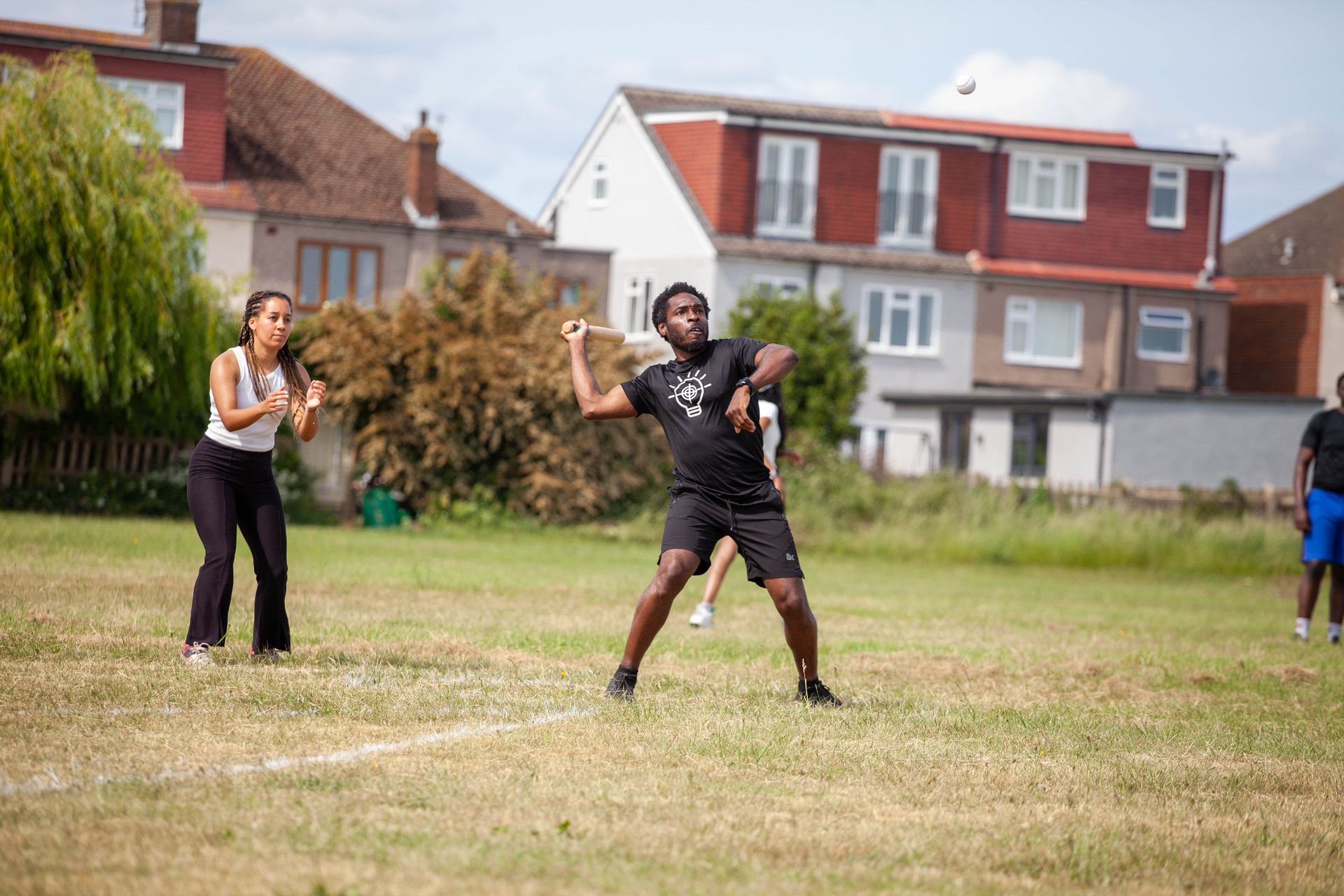 People playing sports in a grassy field in front of houses; one person throws an object.