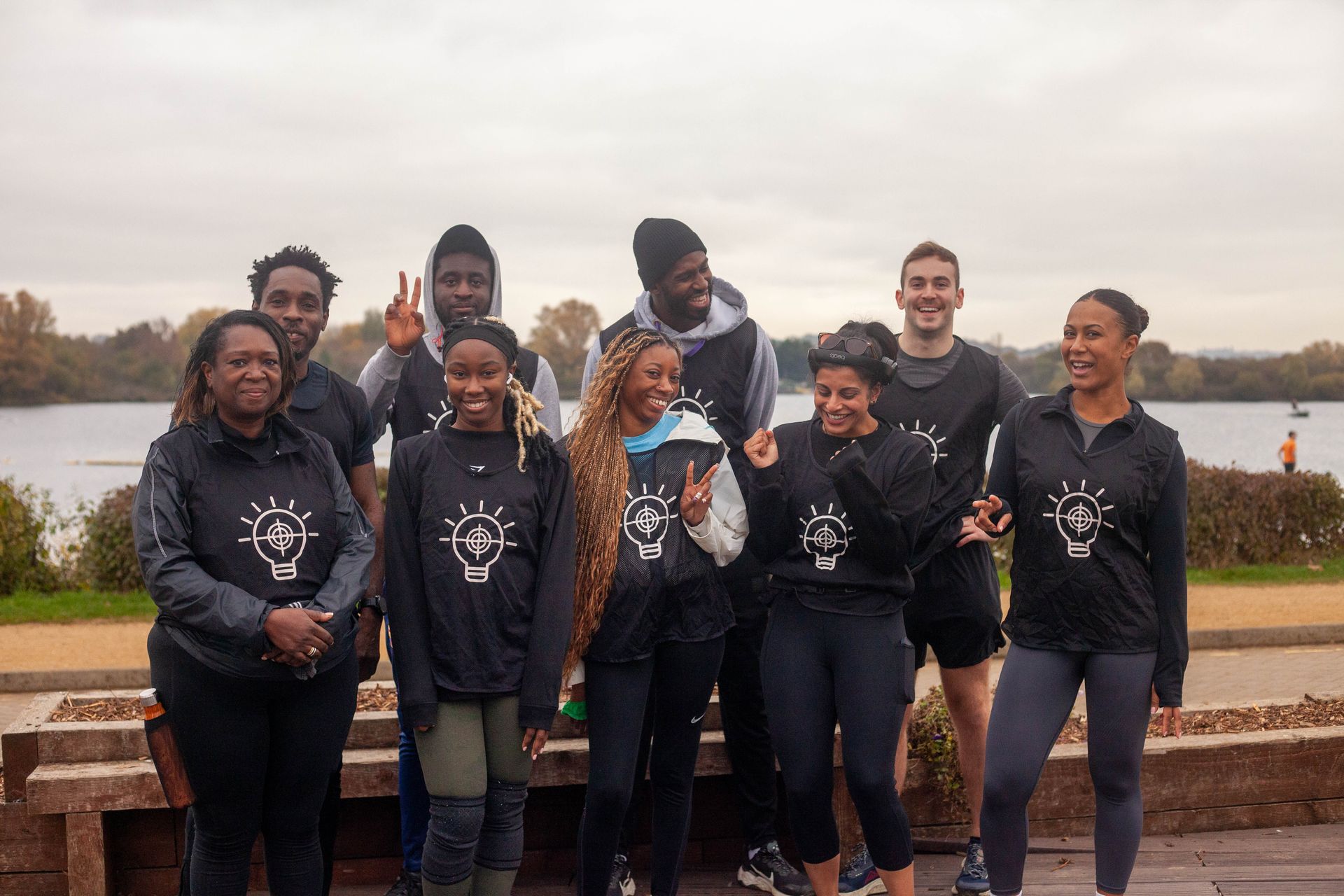 Group of people by water wearing matching black shirts with a lightbulb logo, posing outdoors.