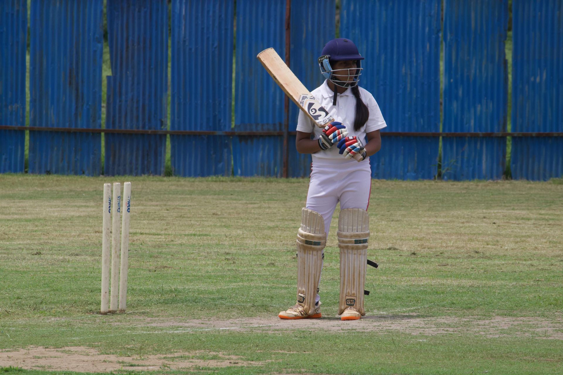 Cricket player in white uniform and helmet, holding a bat, ready to hit.