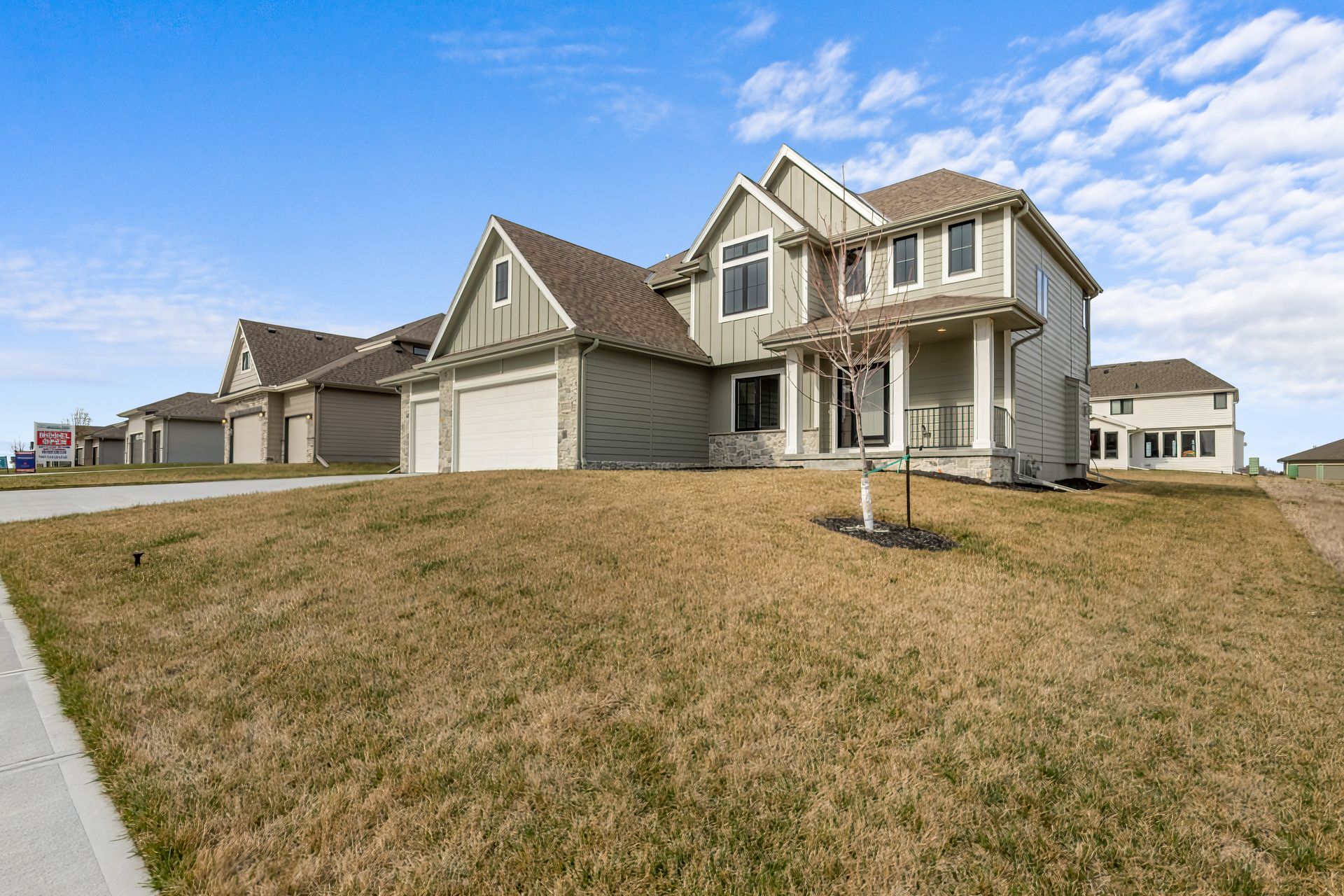 Suburban two-story beige house with attached garage on a grassy hill under a blue sky