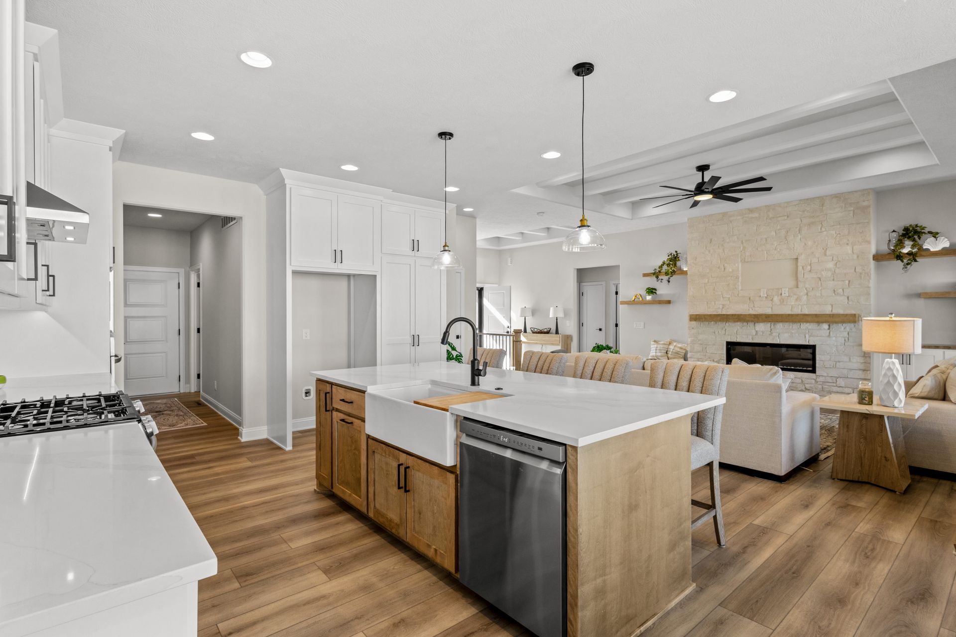 Bright modern kitchen and living room with white cabinets, wood floors, and a stone fireplace