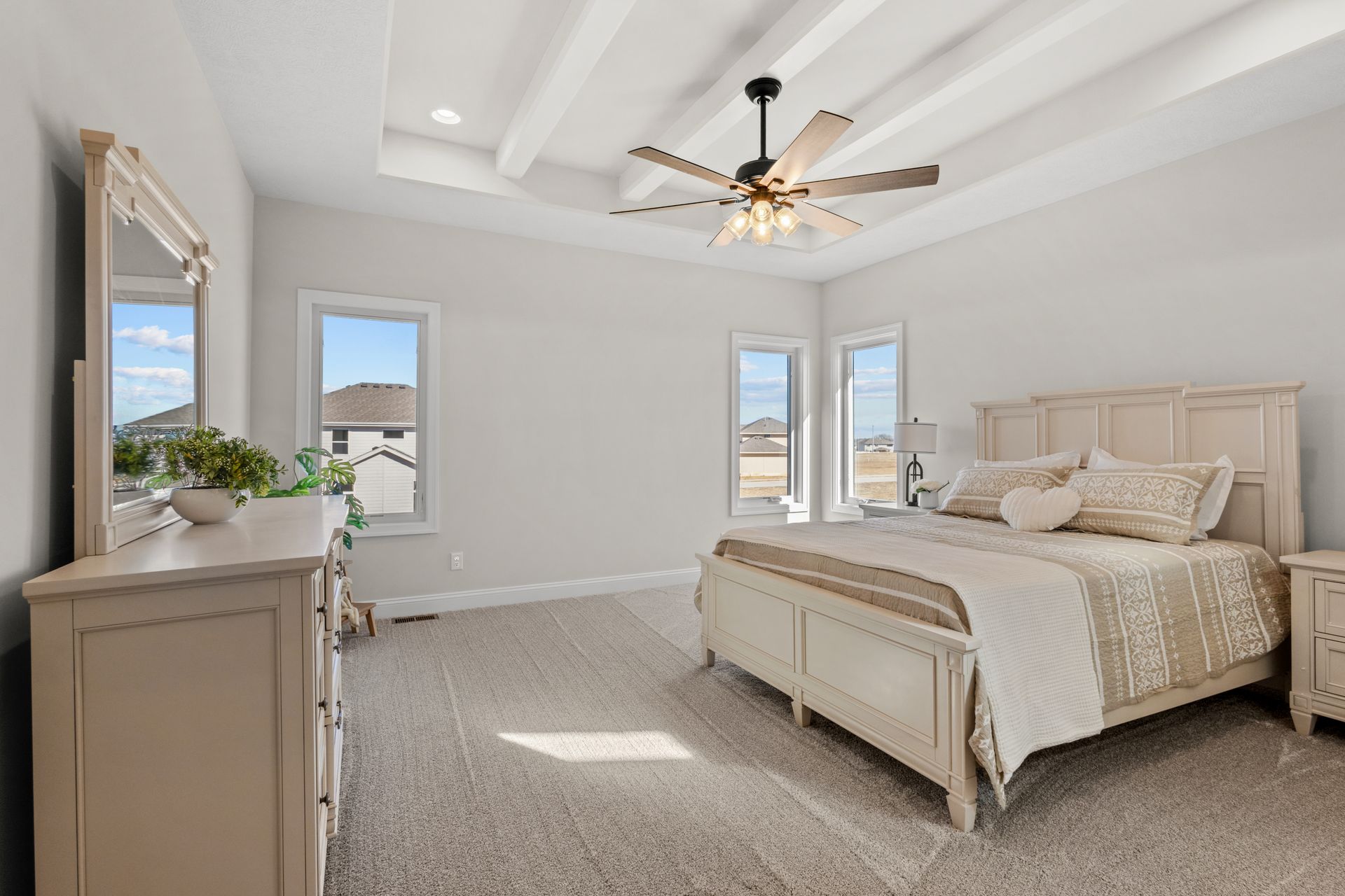 Bright bedroom with a bed, dresser, ceiling fan, and tall windows in soft neutral tones