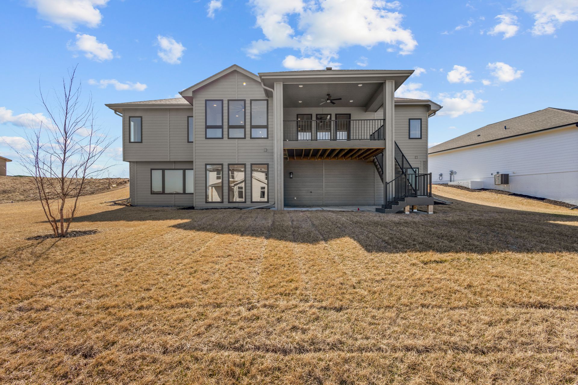 Two-story suburban house with a front balcony, garage, and bare winter lawn under a blue sky