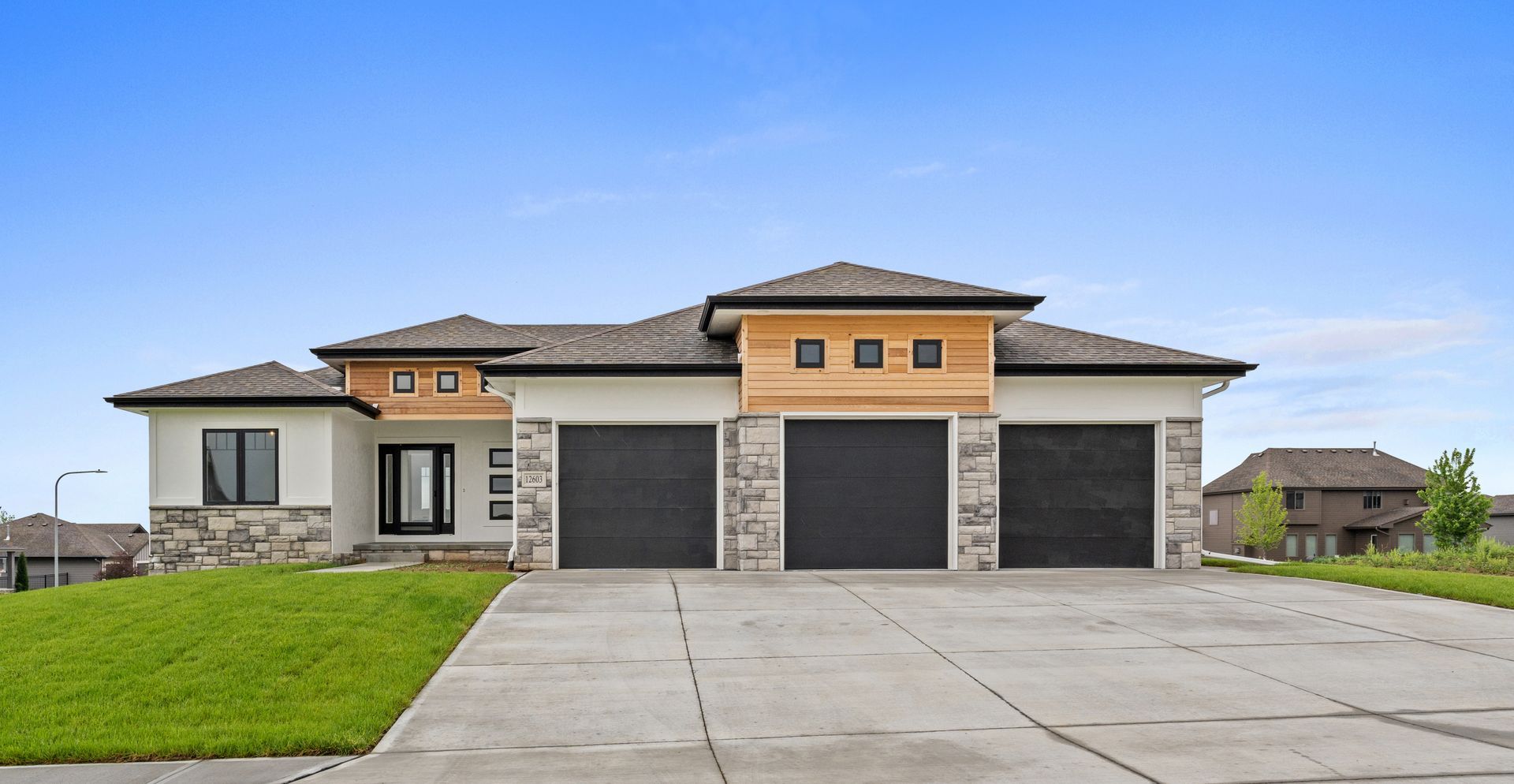 Modern single-story house with three-car garage and wide concrete driveway on a grassy lot