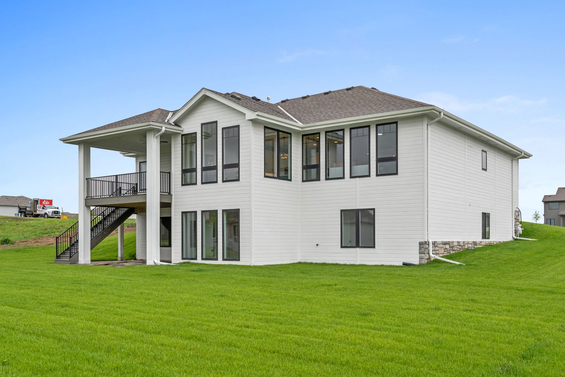 Two-story white house with screened porch on a grassy lot under an overcast sky