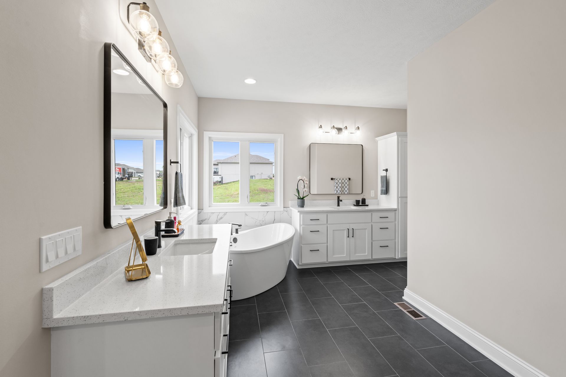Bright modern bathroom with freestanding tub, vanity, large mirror, and black tile floor.