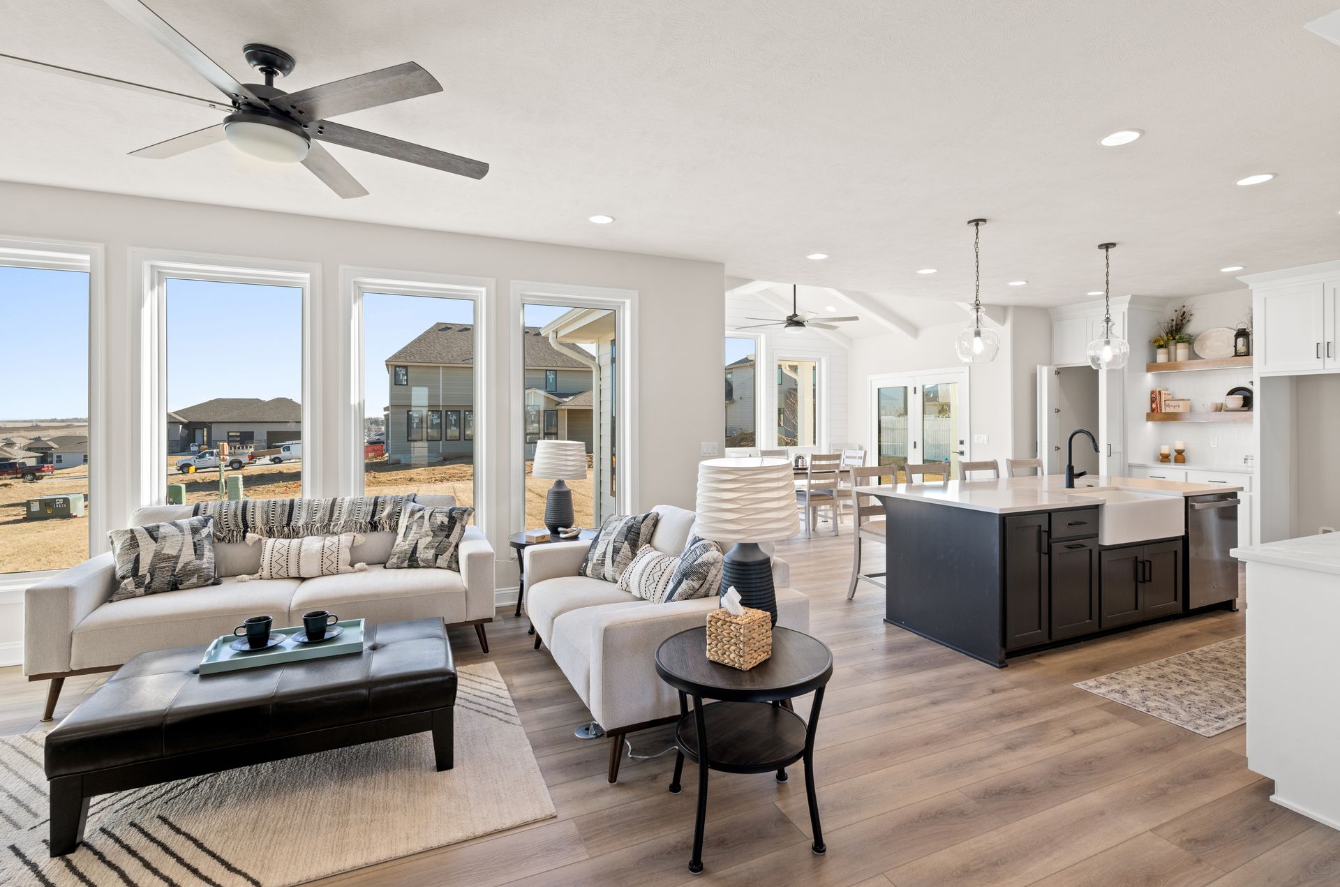 Bright open-plan living room with kitchen island, large windows, and neutral modern furnishings