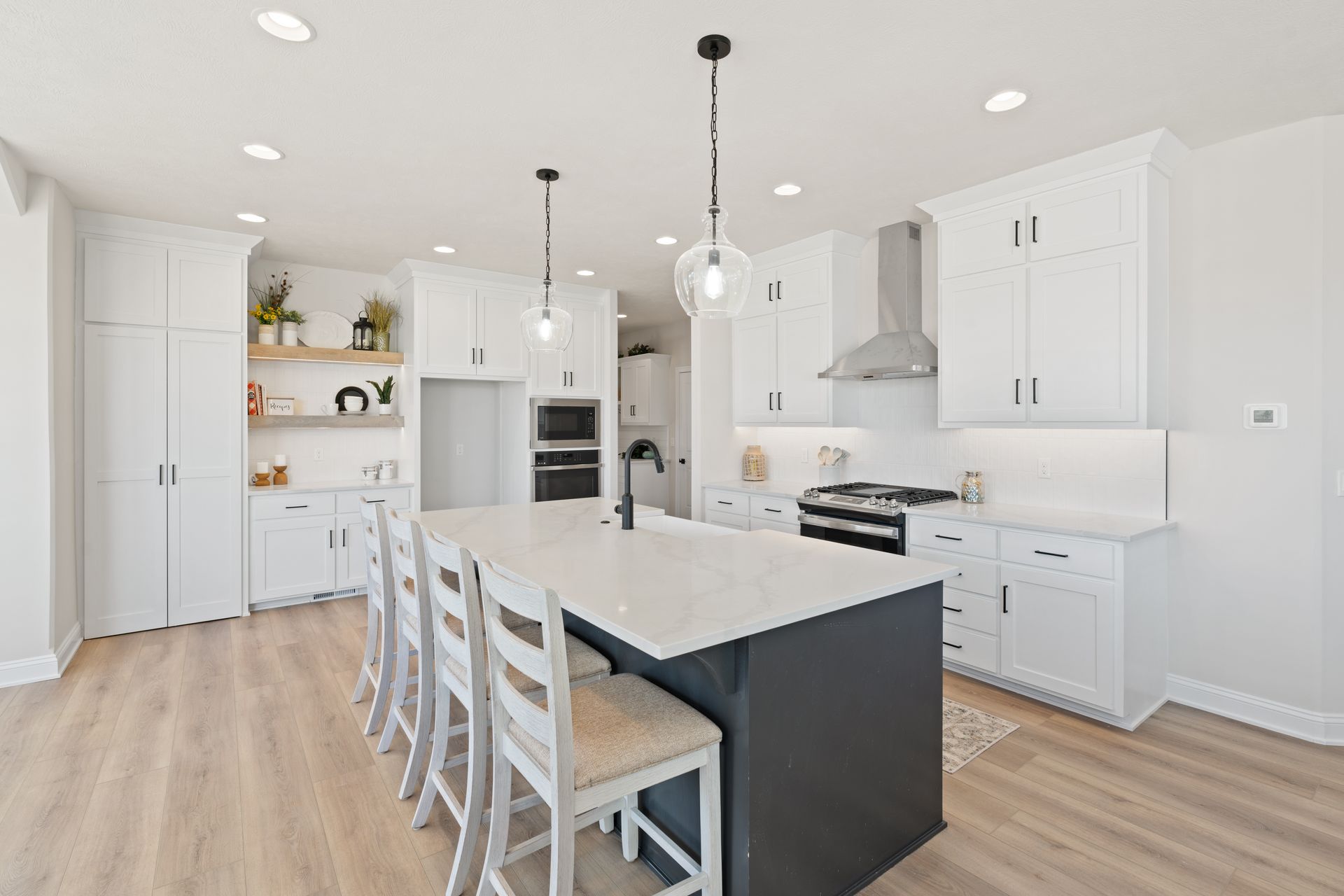 Bright white modern kitchen with island seating, pendant lights, built-in oven, and light wood floors