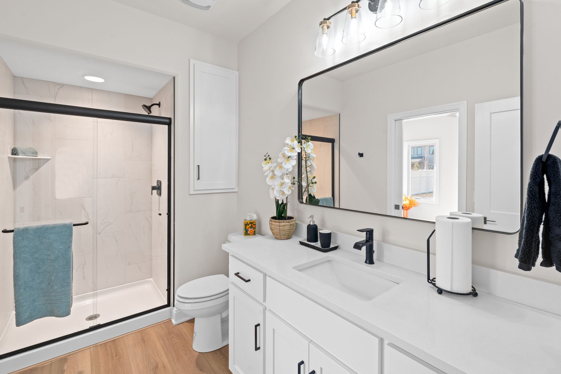 Bright modern bathroom with a glass shower, white vanity, and large mirror