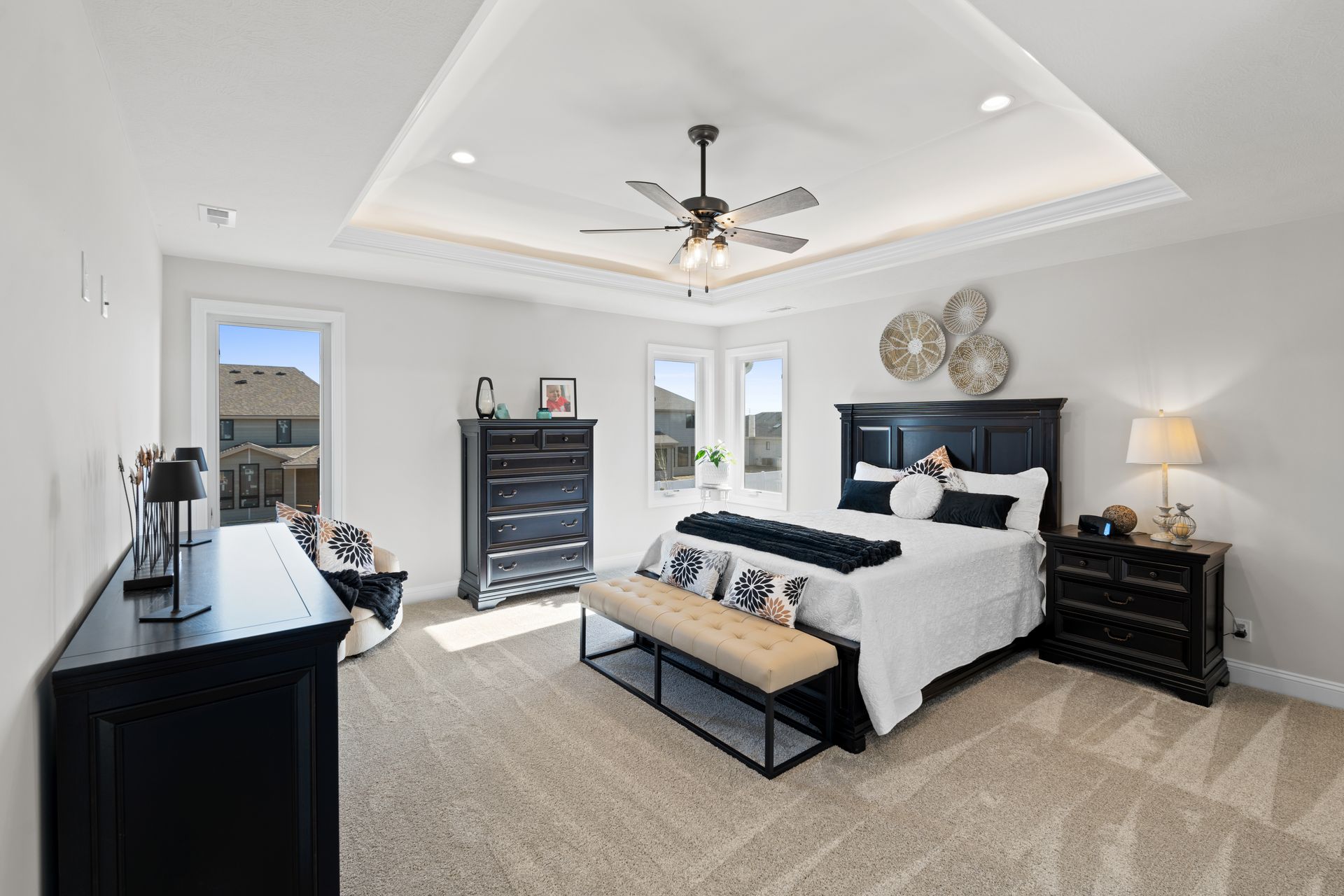 Bright modern bedroom with a large bed, black dresser, ceiling fan, and carpeted floor