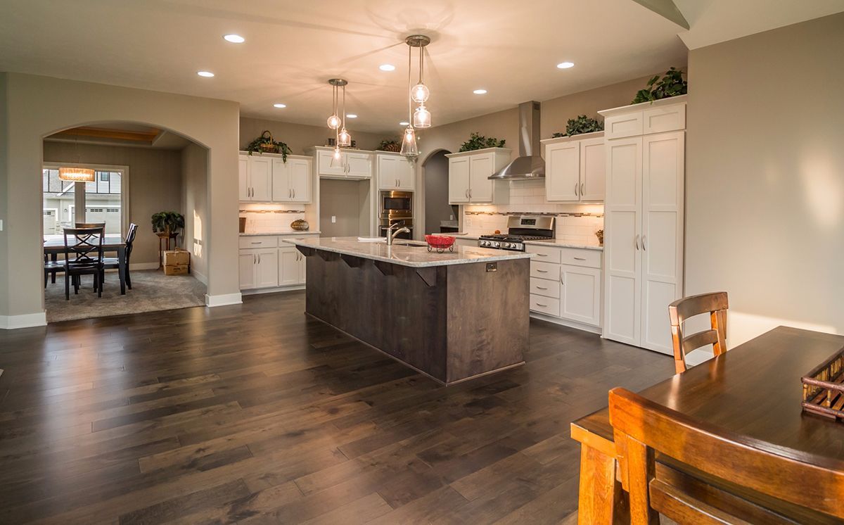 Spacious kitchen with dark wood floors, white cabinets, island, and dining table in the foreground.